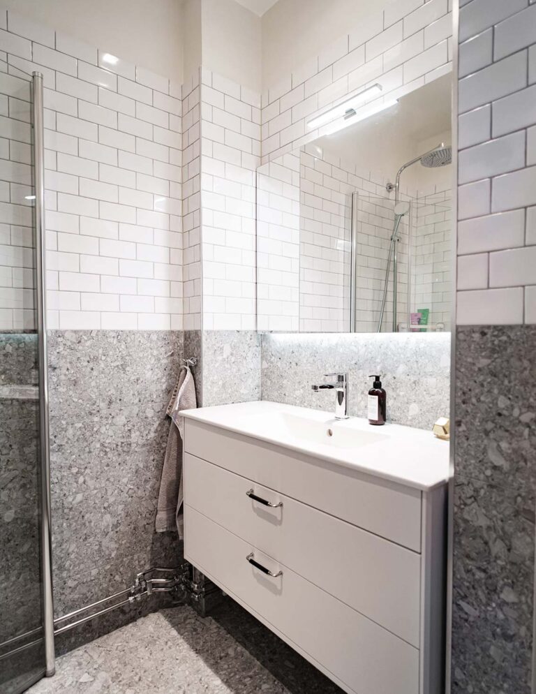 Renoverat badrum med vitt kakel och ljusgrå granit, ett stort vitt handfat med skåp och lyxig belysning