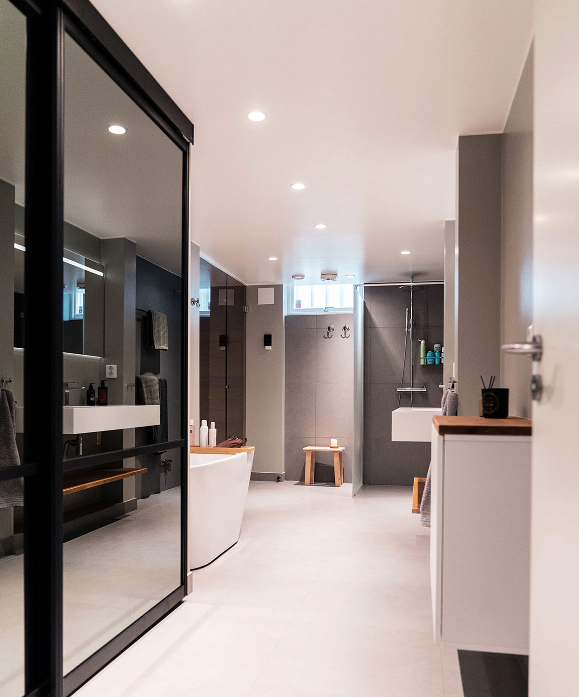 Lyxigt renoverat badrum med badkar, dusch och bastu i svarta, gråa och vita toner med inslag av träelement