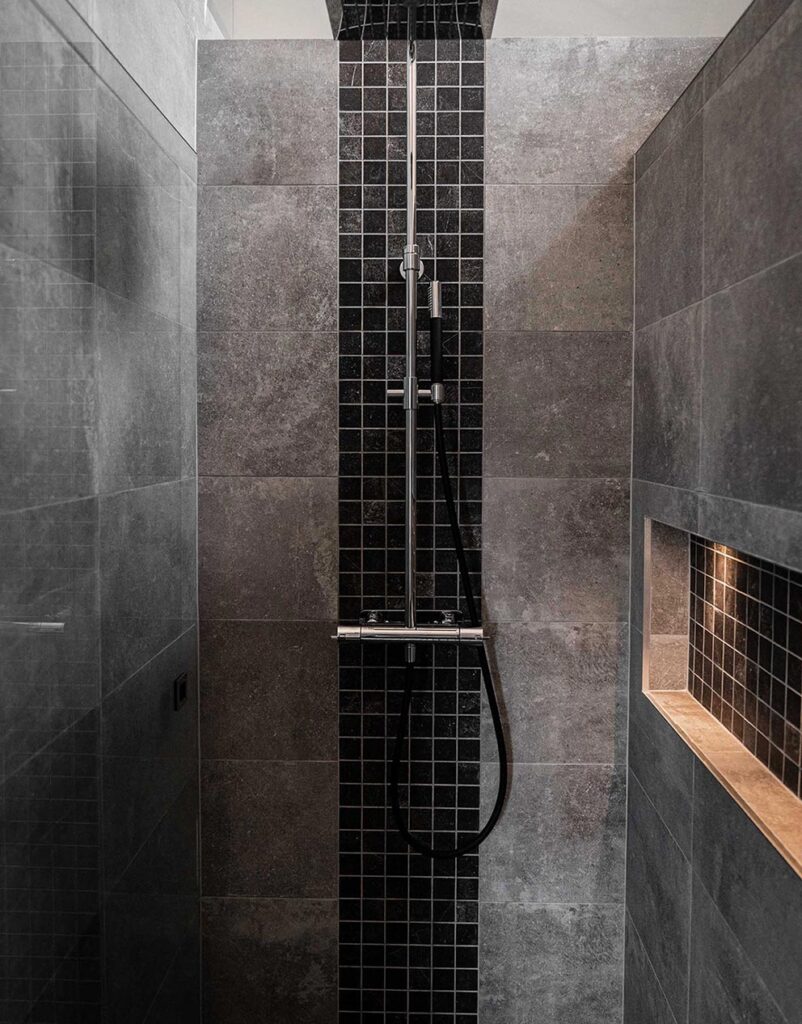 Modern dusch med ljusgrått och svart kakel samt inbyggd belysning i duschen
