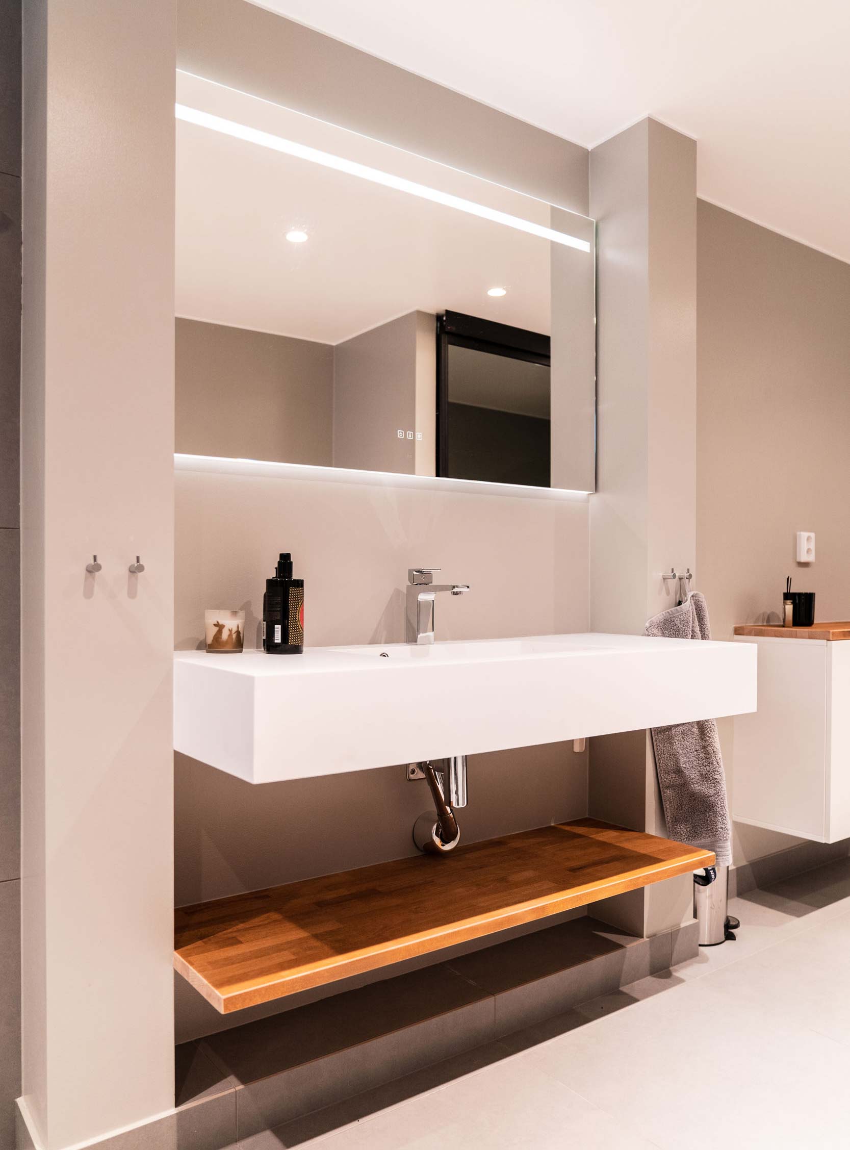 Lyxigt badrum med vitt fyrkantigt stort handfat, lyxig belysning, beiga väggar och detaljer av trä