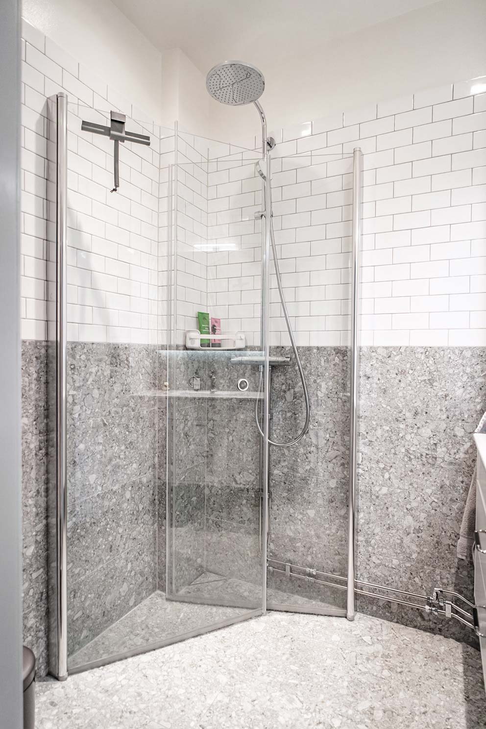 Badrum med vitt kakel och sten på väggarna, en dusch med glasdörrar och ett vattenfallsmunstycke i duschen