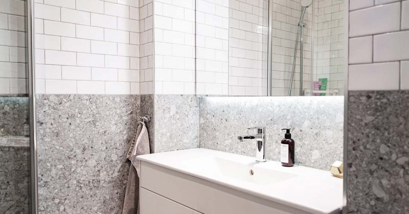 Renoverat badrum med vitt kakel och ljusgrå granit, ett stort vitt handfat med skåp och lyxig belysning