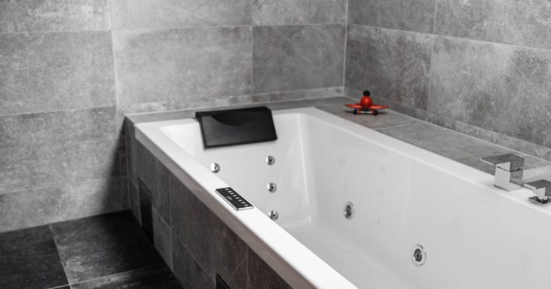 Ett inbyggt badkar med vattenstrålar och massagefunktion, kakel av ljusgrå granit på väggarna och ett snedtak med fönster som släpper in naturligt ljus